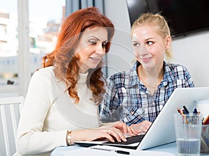 Portrait of mom and daughter at table using laptop together