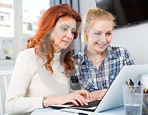 Portrait of mom and daughter at table using laptop together