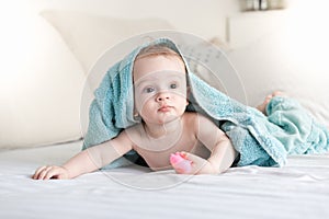 Portrait of cute 9 months old baby boy lying on bed under big blue towel