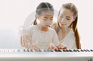 Portrait of mother Asian teaching her daughter playing a piano in living room at home. Spend time weekend together, happy mother