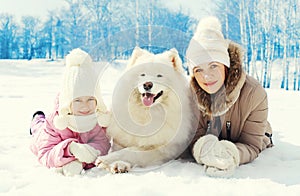 Portrait mother and child with white Samoyed dog together lying on snow in winter