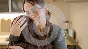 Portrait of mother consoling and stroking her upset daughter crying on kitchen. Parent supporting and comforting child