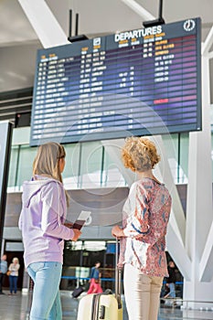 Portrait of mother and daughter looking at flights on monitor in airport