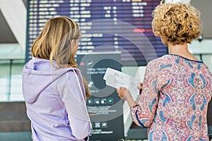 Portrait of mother and daughter looking at flights on monitor in airport