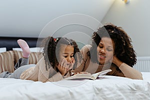 Portrait of mother and daughter reading book while lying on bed at home