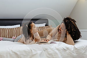 Portrait of mother and daughter reading book while lying on bed at home