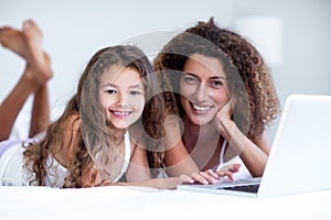 Portrait of mother and daughter using laptop on bed