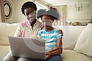 Portrait of mother and daughter using laptop in living room