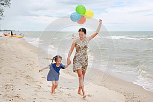 Portrait of Mother and daughter walking on beach with colorful balloons in mother hand. Holiday concept