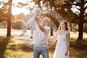 Portrait of a mother, father holds, throws up and spins the daughter on hands walking on nature on summer day vacation. Mom, dad