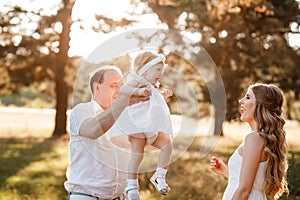 Portrait of a mother, father holds, throws up and spins the daughter on hands walking on nature on summer day vacation. Mom, dad