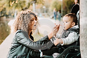 Portrait of mother feeding yogurt to 1 year old baby in stroller