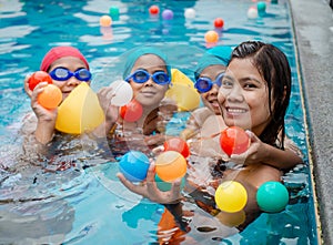 A portrait of a mother and her children playing ball in the pool