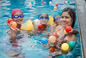 A portrait of a mother and her children playing ball in the pool