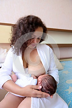 Portrait of a mother and her cute newborn baby. Happy mom smiles looking at her baby boy while breastfeeding him