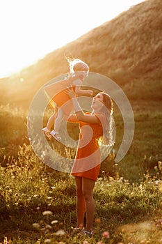 Portrait of a mother holds, throws up and spins the daughter on hands on nature on summer day vacation. Mom and girl playing in