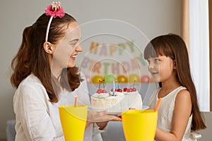 Portrait of mother and little girl celebrating birthday with delicious cake for her little daughter, waiting to blow the candles