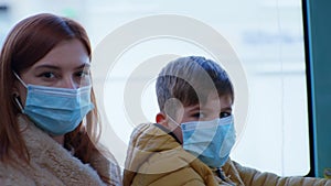Portrait of mother with male child wearing medical masks to protect against coronavirus while traveling on public bus