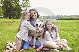 Portrait of a mother and two daughters with a husky dog smiling looking at the camera in a summer park.