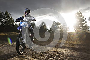 A portrait of motocross rider sitiing on the bike on the background of sunset