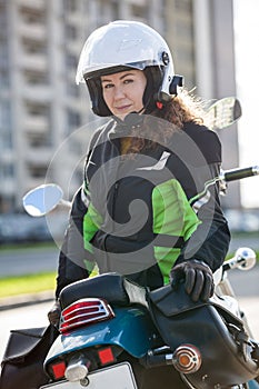 Portrait of motorbiker Caucasian woman in white open face crash helmet and touring jacket sitting on motorcycle