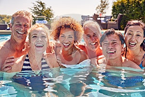 Portrait Of Multi-Cultural Group Of Senior Friends Relaxing In Outdoor Pool On Summer Vacation