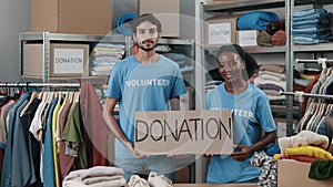 Portrait of multi ethnic colleagues looking at the camera and smiling while holding banner with donation word in charity
