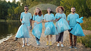 Portrait of multi-ethnic group of volunteers with bin bags on clean lake shore