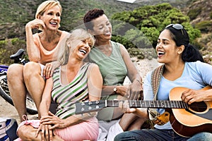 Portrait of multi ethnic old friends singing while playing guitar on the beach