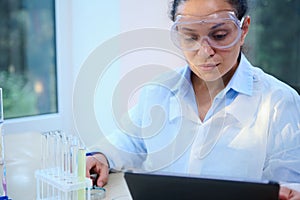 Portrait of a multi-ethnic woman, scientist in protective goggles working on a digital tablet in a medical laboratory