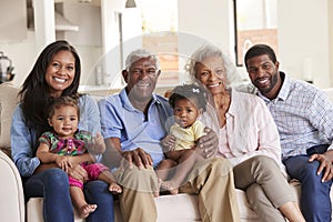 Portrait Of Multi-Generation Family Sitting On Sofa At Home With Baby Granddaughters