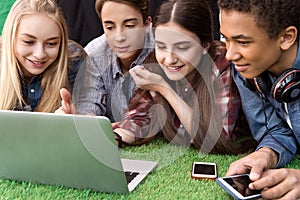 portrait of multicultural smiling teenagers using laptop and smartphones together while resting photo