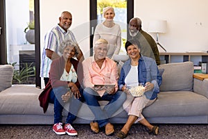 Portrait of multiracial senior friends with digital tablet and popcorns enjoying in nursing home