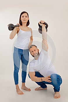 Portrait of muscular barefoot family wearing white T-shirts, blue jeans, showing muscles. Woman holding kettle bell.