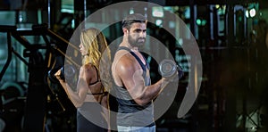 Portrait of muscular couple gym trainers using dumbbell inside gym with dark tone background for exercise and workout concept