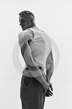 Portrait of muscular male fashion model wearing white t-shirt and posing over studio background. Monochrome, back view