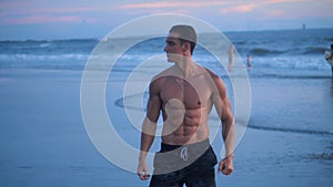 Portrait of muscular man with a naked torso on the beach at sunset.