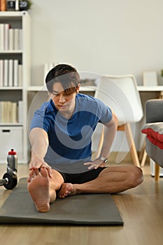 Portrait of muscular man in sportswear stretching his legs, warming up exercises before working out at home