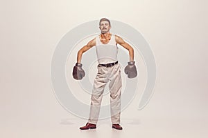 Portrait of muscular man in vintage clothes showing muscles in boxing gloves, posing isolated over grey studio