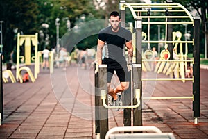 Portrait of muscular man working out in park, triceps workout at special training zone