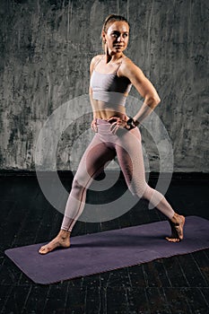 Portrait of muscular young athletic woman with perfect beautiful body in activewear holding hands on waist and lunging