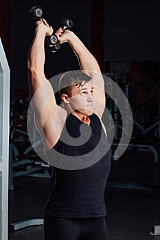 Portrait of a muscular young man lifting weights on gym background. hard training,