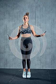 Portrait of muscular young woman exercising with jumping rope on grey background.