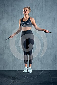 Portrait of muscular young woman exercising with jumping rope on grey background.