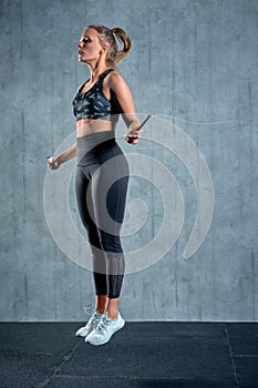 Portrait of muscular young woman exercising with jumping rope on grey background.