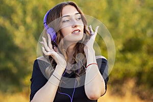 Portrait of a music lover teenager girl in headphones, young woman listening to lovely song on the nature in the field