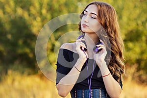 Portrait of a music lover teenager girl in headphones, young woman listening to lovely song on the nature in the field