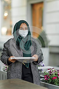 Portrait of a muslim girl in a face mask with a laptop on the street