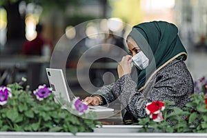 Portrait of a muslim girl in a face mask with a laptop in the street cafe