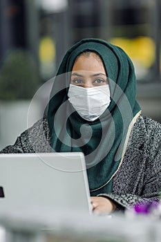 Portrait of a muslim girl in a face mask with a laptop in the street cafe